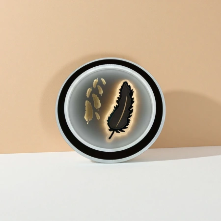 The circular lamp with black borders and white frames is decorated with golden feathers and features a black luminous feather shape The circular lamp with black borders and white frames is decorated with golden feathers and features a black luminous feather shape